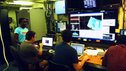 Kandice from the night shift visits the three men during their day watch. We monitor the multibeam system on the big screen; but the 'heart' of the system that does all the math, and real-time processing, is hidden in the unimpressive, grey box in the back. / Kandice von der Nachtwache besucht die drei Männer der Tagwache. Das Multibeam-System wird über den großen Bildschirm überwacht, wobei sich das eigentliche Herzstück des Systems, die Steuer- und Prozessiereinheit, in dem unscheinbaren, grauen Kasten im Hintergrund versteckt. (Photo by Meike)