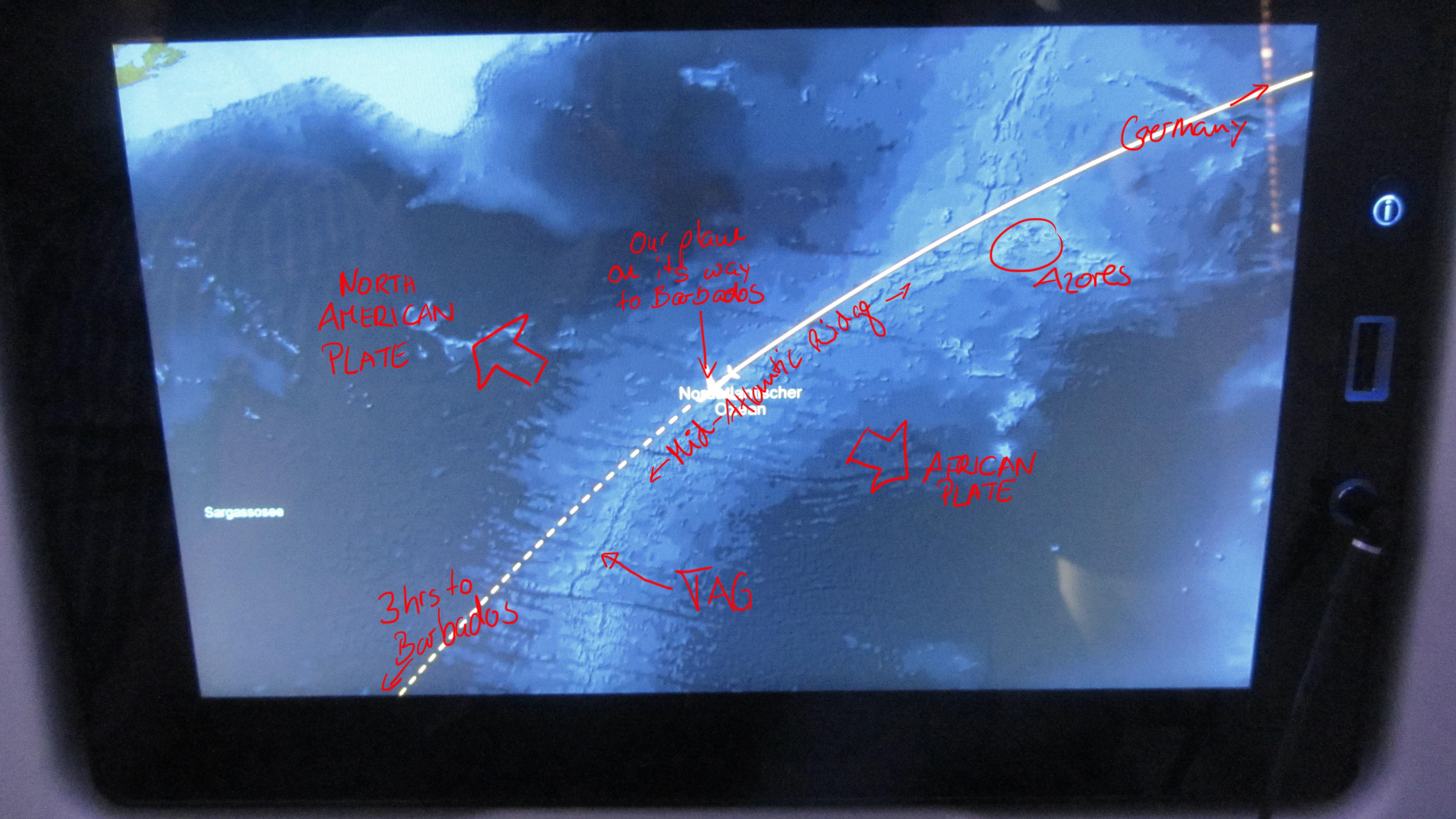 Photo of the info screen on our flight to Barbados with some remarks on what marine geologists see on it: The Mid-Atlantic Ridge (in pale blue colours, as it is shallower than the deep sea plains in dark blue) is a boundary, at which two tectonic plates spread apart. The North American plate, including the continent, moves with a rate of 1cm per year west, while the African and Eurasian plate move with also about 1 cm per year eastwards. The TAG hydrothermal field lies on the plate boundary, which is visible as a fine blue line, due to a graben structure, the so-called rift valley, on top of the Mid-Atlantic Ridge. / Foto vom Infobildschirm auf unserem Flug nach Barbados mit einigen Anmerkungen, was Meeresgeologen darauf sehen: Der Mittelatlantische Rücken (als hellblaues Band gut sichtbar, weil er sich von den tiefer gelegenen Tiefseeebenen in dunkelblau abhebt) ist eine Grenze, an der zwei tektonische Platten auseinander spreizen. Die Nordamerikanische Platte, inklusive des Kontinents, bewegt sich mit rund 1 cm pro Jahr nach Westen, während die Eurasische und Afrikanische Platte mit ebenfalls 1 cm pro Jahr nach Osten driften. Das TAG Hydrothermalfeld liegt genau auf der Plattengrenze, die als feine, dunkelblaue Linie auf dem Mittelatlantischen Rücken sichtbar ist, weil sich dort ein tiefer gelegener Graben befindet, das so genannte Rift Valley. (© Meike Klischies)