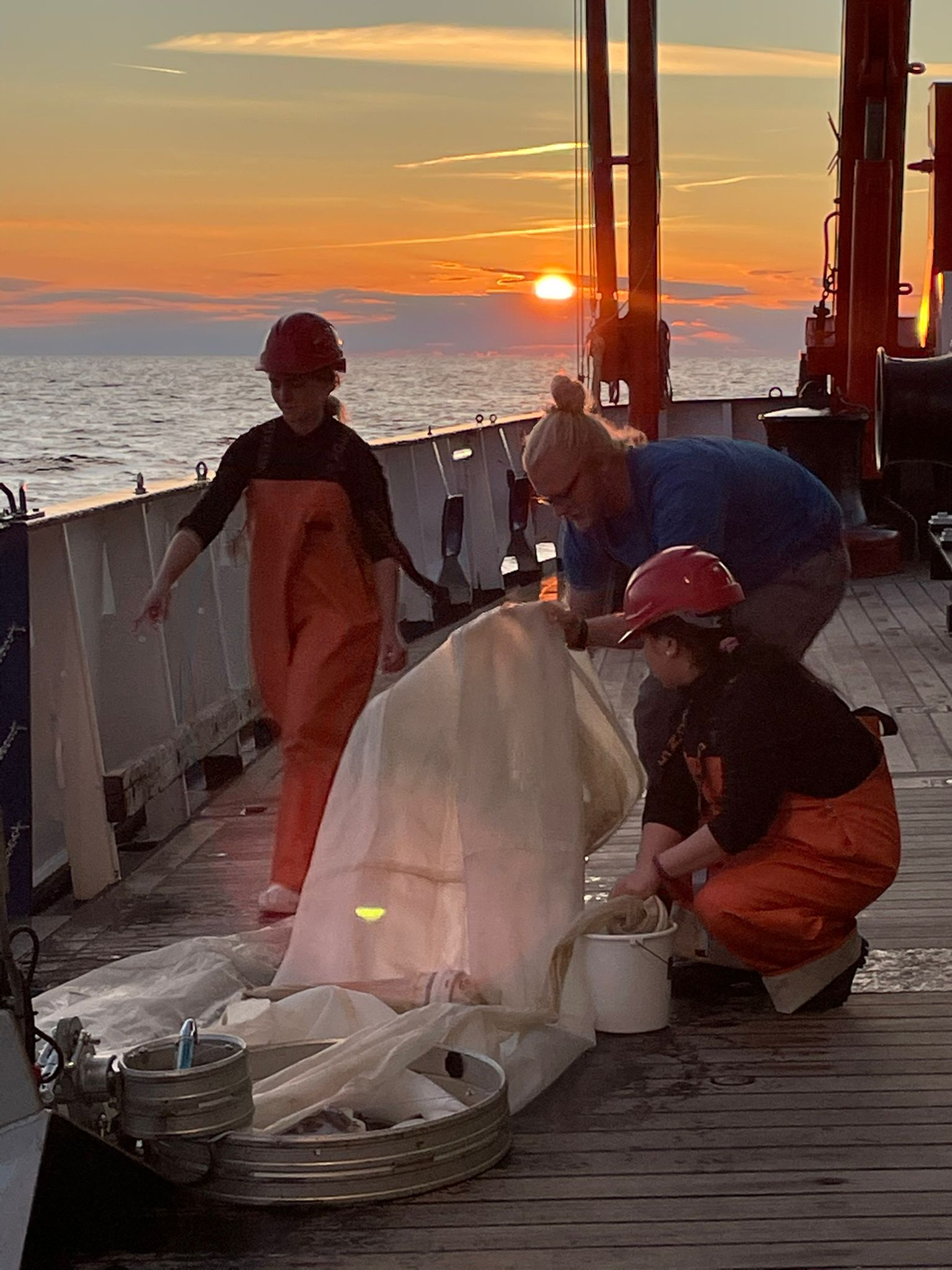 Scientist onboard RV Alkor work on deck with the mulitnet, sunset in the background